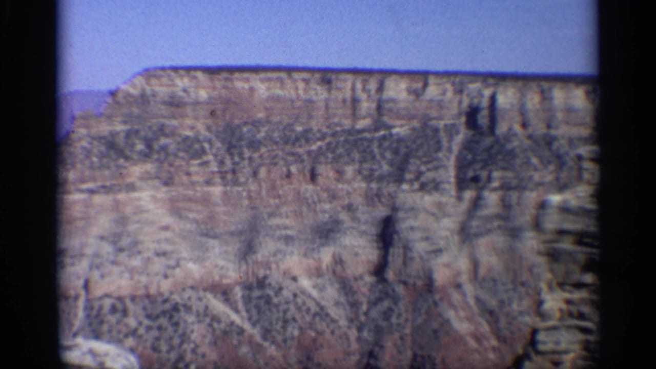 Wide canyon wall with layered cliffs under a pale blue sky.