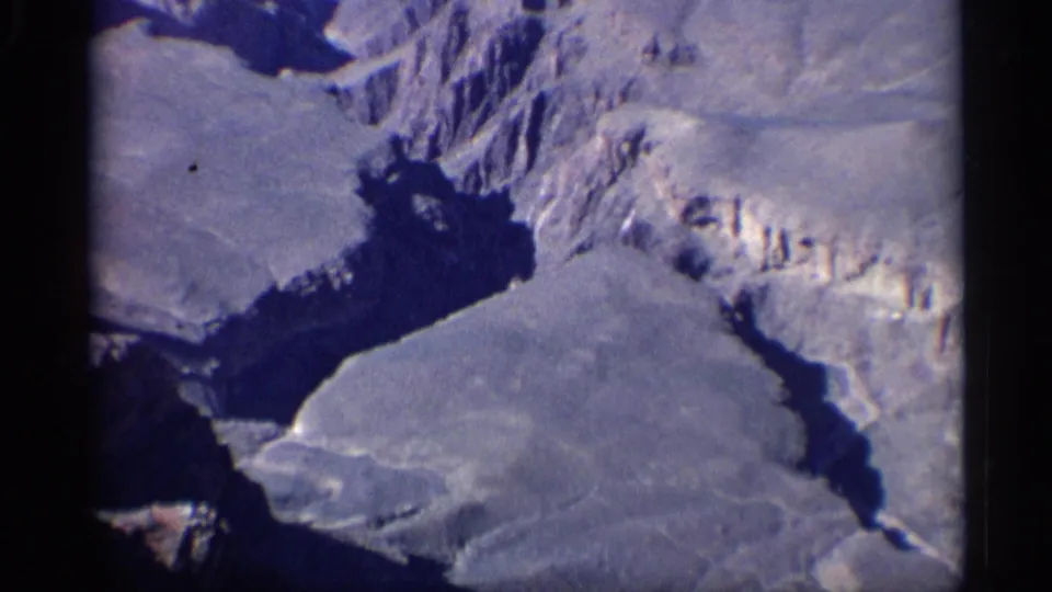 Arizona home-movie frame looking down into a dry canyon area with steep rocky slopes and a broad dark shadow.