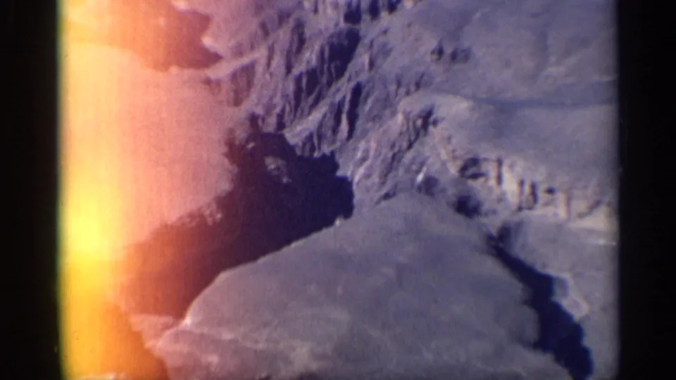 1959 Arizona 8mm view of dry canyon ridges and a dark ravine, with warm light flare and visible film border.