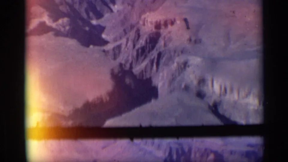 1959 Arizona 8mm frame showing rugged canyon walls, dry rock shelves, a dark basin, and visible film gate edges.