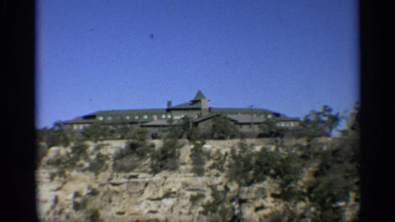 Rim building viewed across rocky foreground and sparse trees.