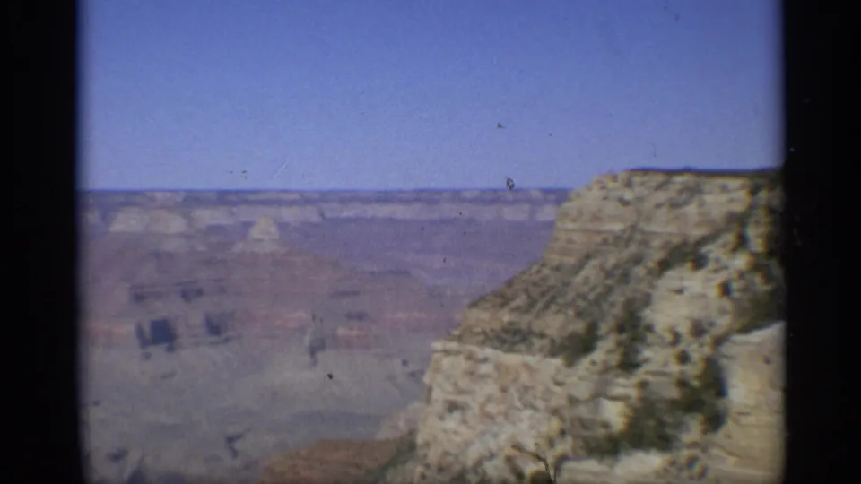 Hazy 1959 Arizona 8mm view across the Grand Canyon, with a pale rock outcrop in the foreground and distant layered formations.
