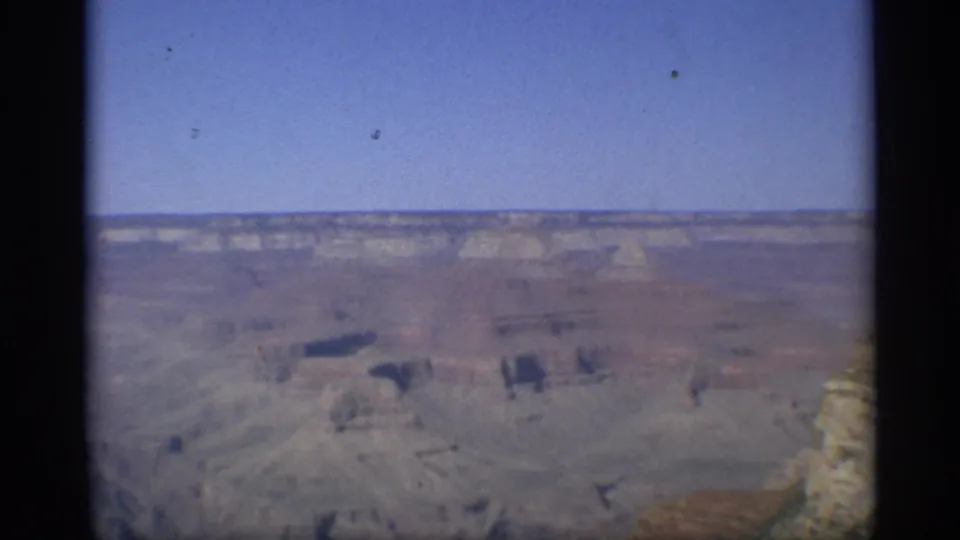 Wide Grand Canyon panorama from a 1959 Arizona home movie, showing distant cliffs, muted rock layers, and a rim edge at the right.