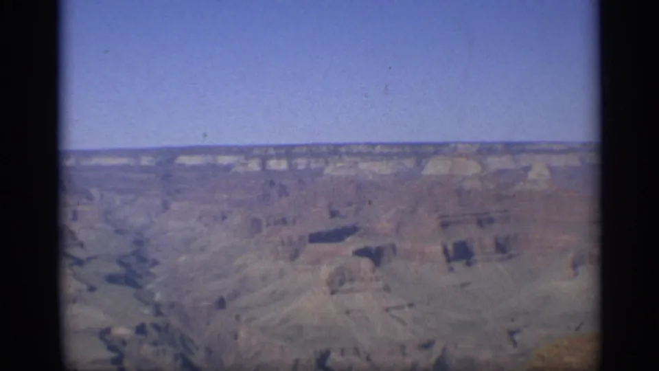 1959 8mm Arizona footage shows a distant Grand Canyon panorama with pale blue sky, stratified rim, and shadowed rock formations.
