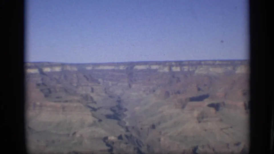 The 1959 Arizona home-movie frame shows Grand Canyon layers and dark ravines seen from a distant overlook.
