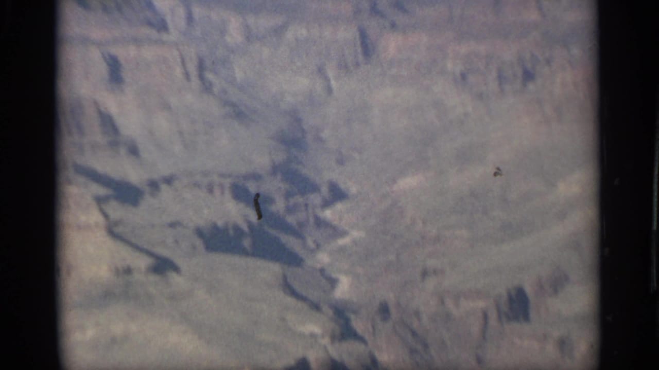 Soft aerial view of pale canyon terrain with dark ravines and film-edge shadow.