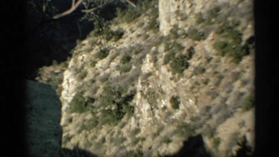 Arizona desert rock formation with scrub vegetation and a dark shadowed recess, captured on 8mm film.