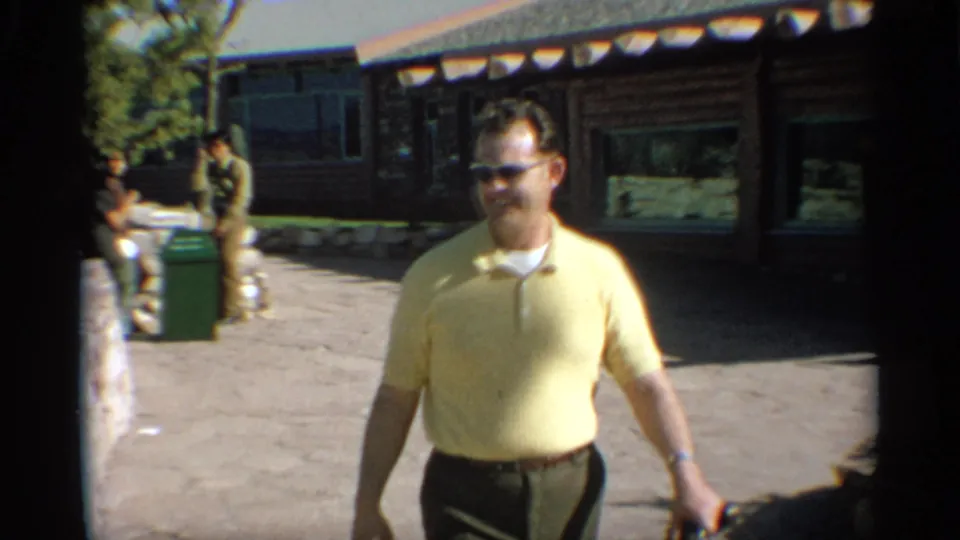 A closer 1959 Arizona frame shows the man in sunglasses passing the camera, with the cabin and background visitors behind him.