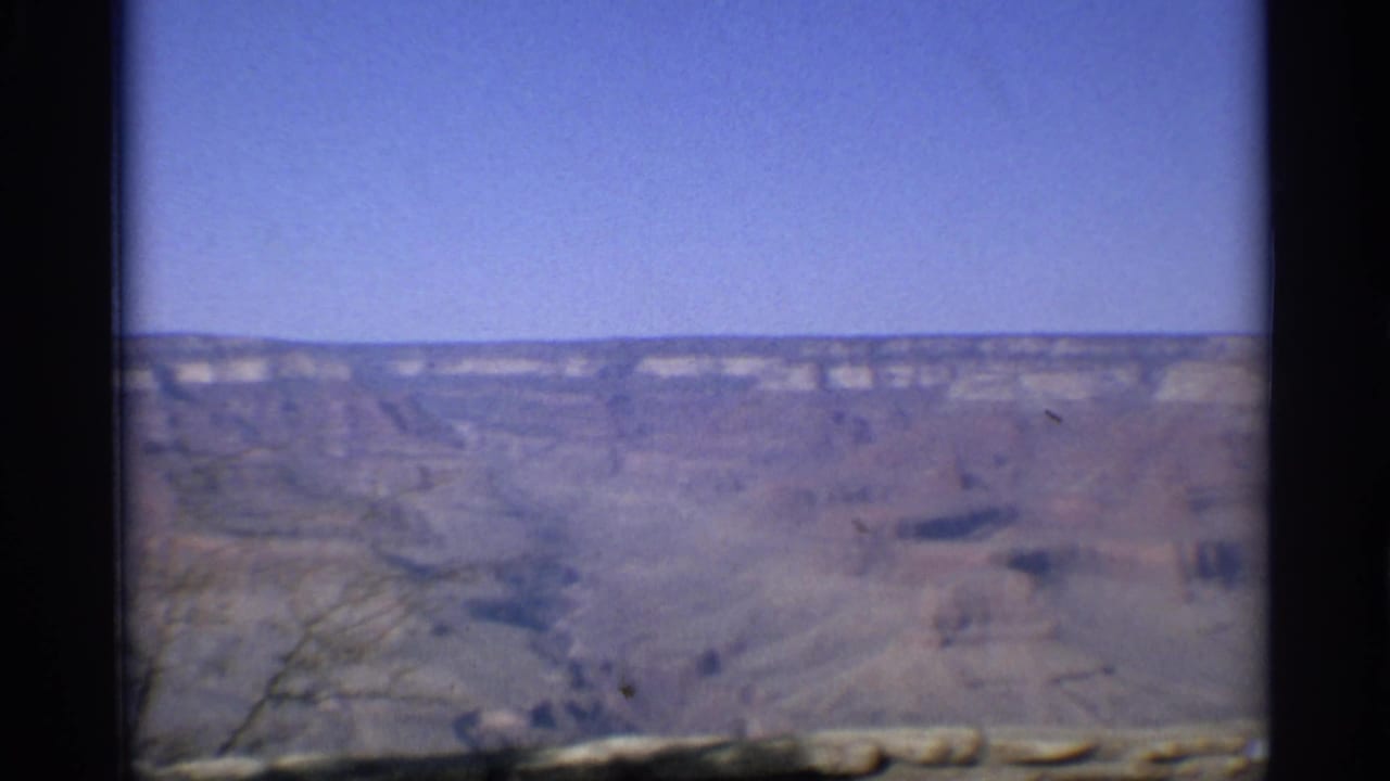 Soft 8mm view across a canyon beneath a clear blue sky with dark film borders.