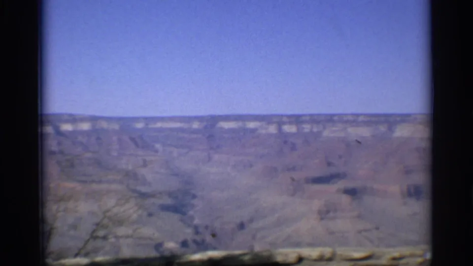 1959 Arizona 8mm frame showing a distant Grand Canyon overlook view with layered rock walls, blue sky, and visible film-gate edges.