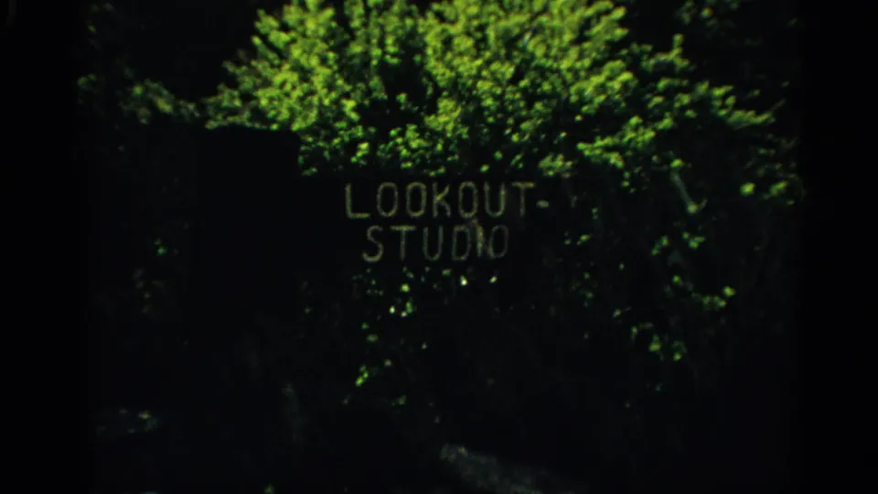 Dim 1959 Arizona frame with the Lookout Studio sign visible behind leaves and deep shadow.