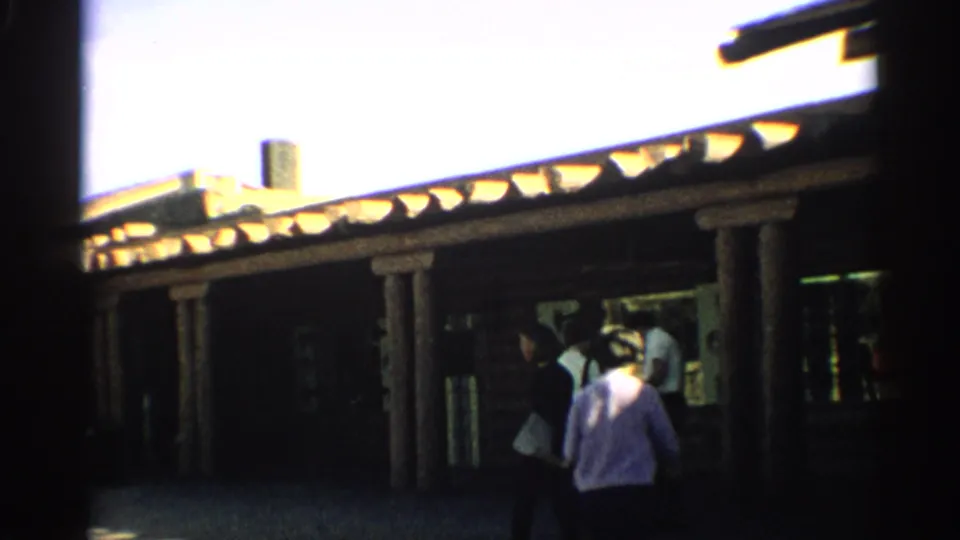 1959 Arizona 8mm frame of a rustic wooden building exterior with visitors gathered under a covered porch.