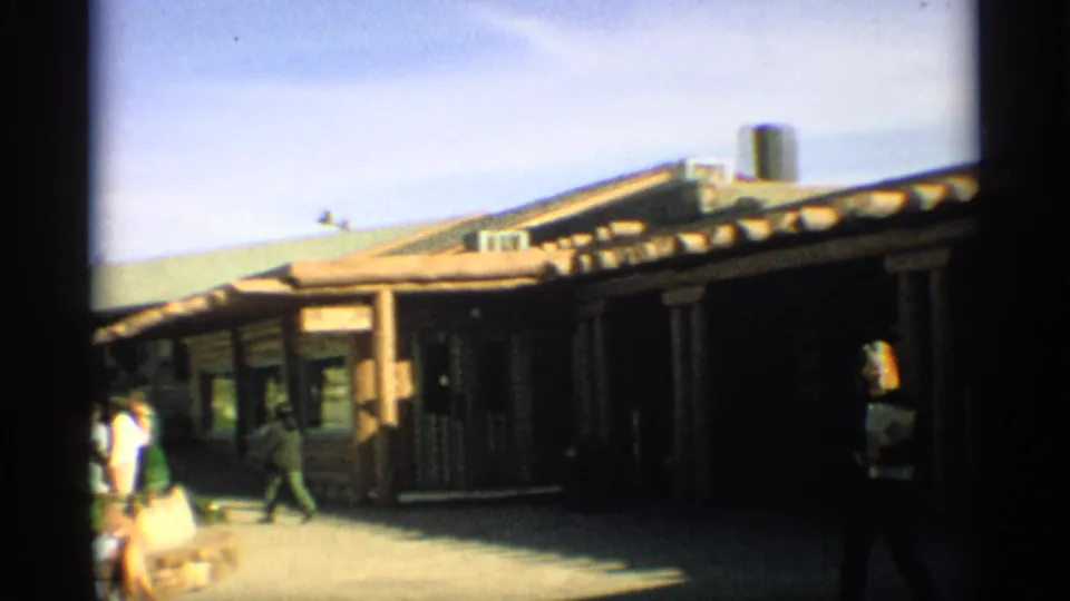 1959 Arizona exterior view of a rustic studio building with visitors crossing a bright walkway.