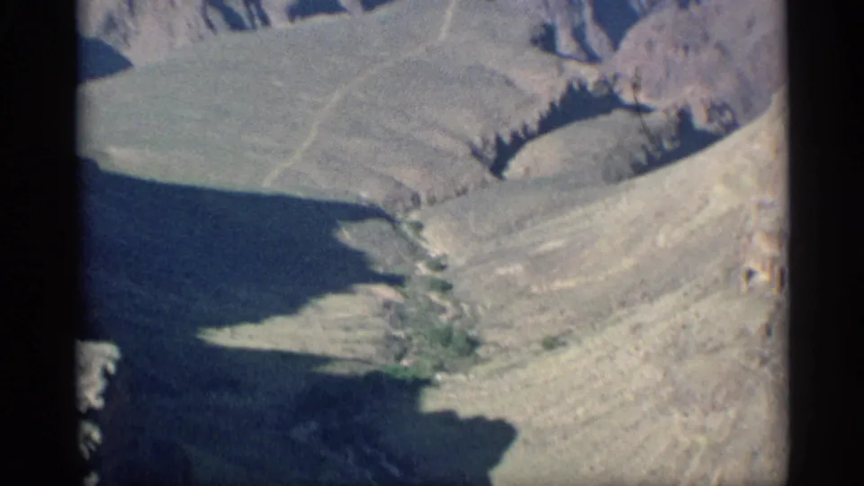 1959 Arizona 8mm aerial view crossing a rocky canyon slope, with shadowed terrain and faint wash lines below.
