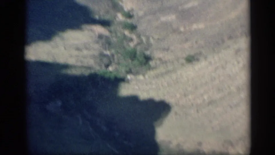 1959 Arizona aerial frame with a blurred canyon edge, dark basin shadow, pale rock, and a narrow green wash.