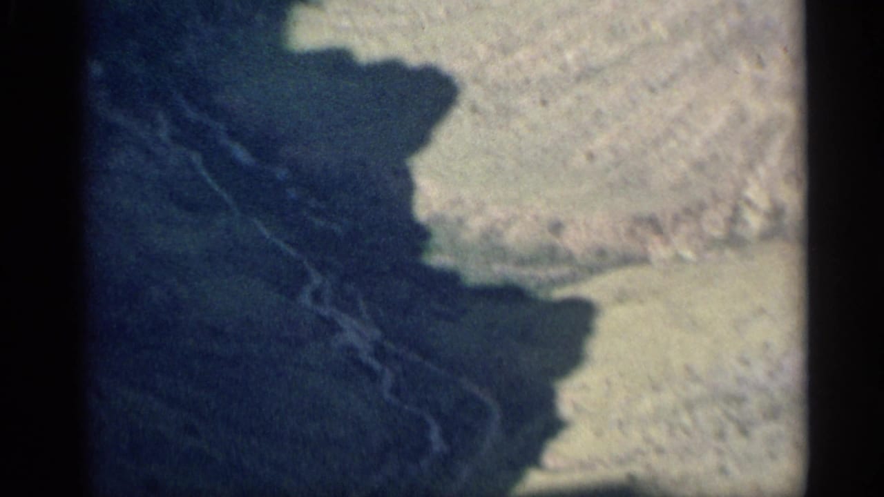 Shadowed rocky terrain beside a pale hillside, bordered by dark 8mm film edges.