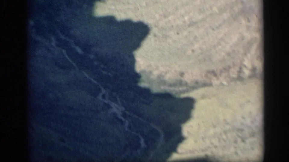 1959 Arizona home-movie frame showing shadowed rugged terrain and a pale rocky slope through soft, dark-edged 8mm exposure.