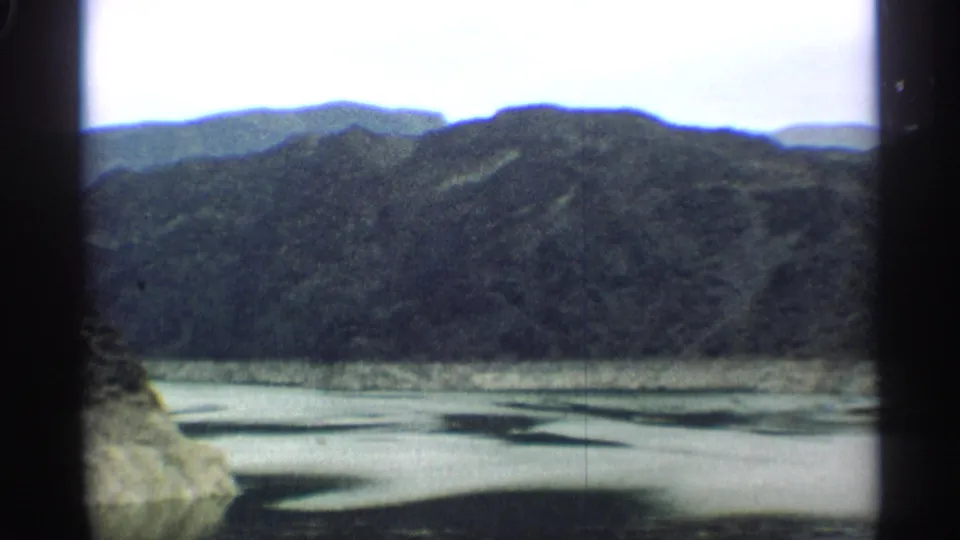 1959 Arizona 8mm frame looking across a reservoir or river bend toward dark hills and distant ridgelines.