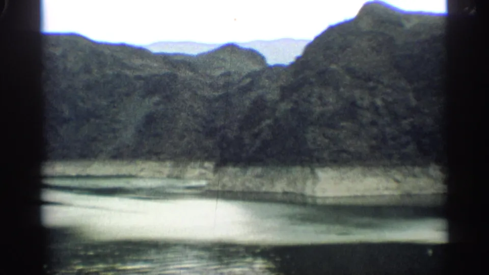 1959 Arizona home-movie landscape with dark mountain ridges, pale water, and a soft blue-green 8mm color cast.