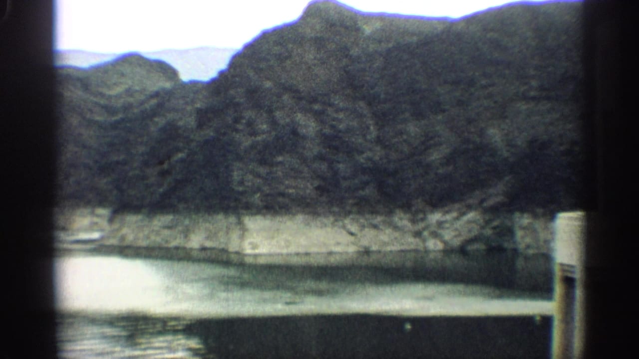 Reservoir water, canyon slopes, and a small dam tower seen through soft 8mm framing.