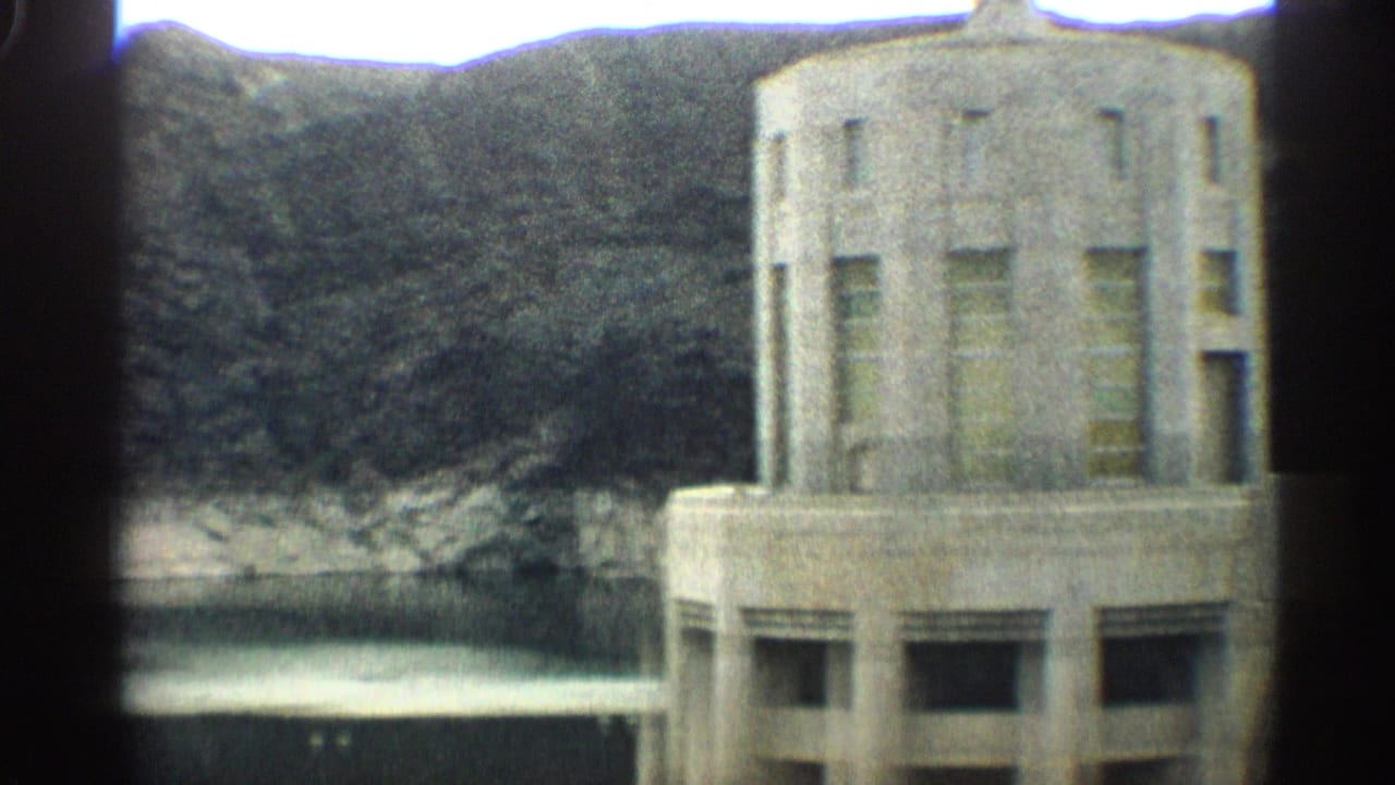 Close view of a tall concrete dam tower with canyon and water behind it.