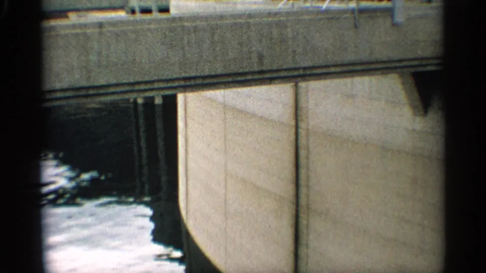 1959 Arizona 8mm frame showing a close view of a concrete dam wall with water moving below and dark film-edge framing.