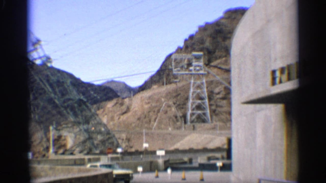Desert mountains, transmission tower, roadway, and concrete dam edge.