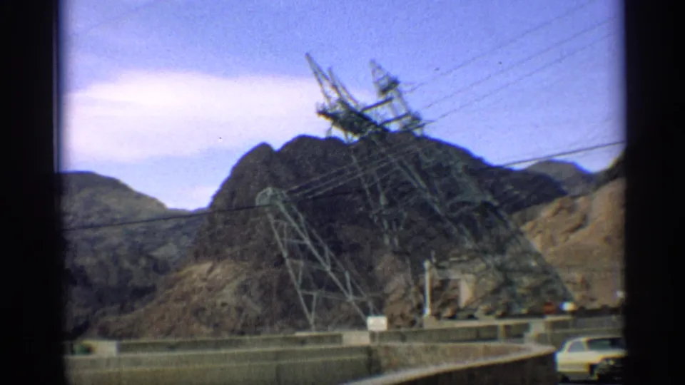 1959 Arizona frame showing power transmission towers and wires over desert mountains, with a roadway and partial car at the lower edge.