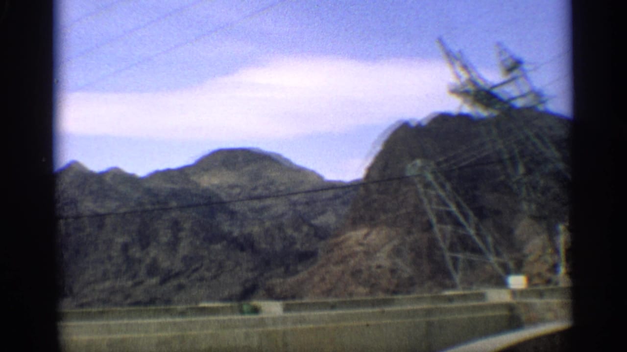 Desert mountains, power lines, a transmission tower, and a concrete structure seen through film-frame borders.