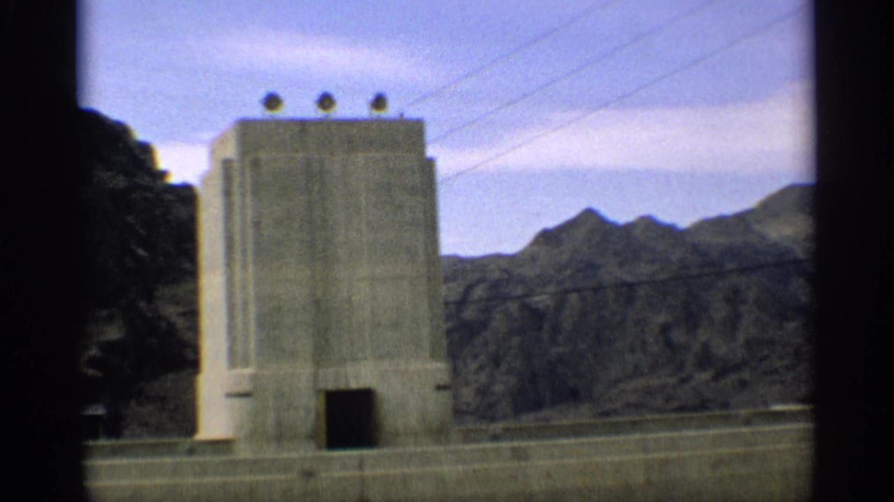 Tall concrete structure with dark doorway, power lines, and rocky mountains in the background.