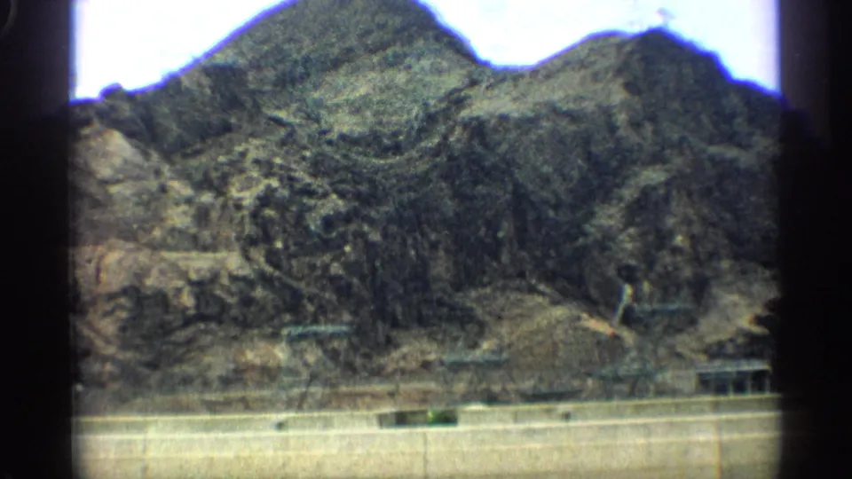 1959 Arizona 8mm frame of rugged desert mountains crossed by power lines, with a small structure near the lower edge of the frame.