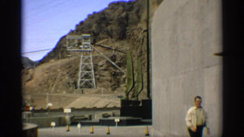 Adult man stands near a concrete structure at an Arizona utility site, with tower equipment and desert hills behind him.