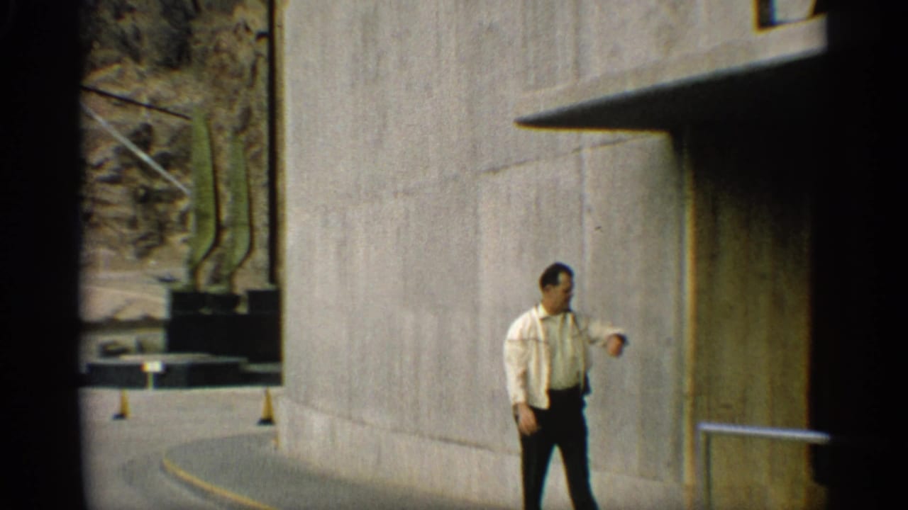 Man walking beside a tall concrete wall near a railing and curved roadway.