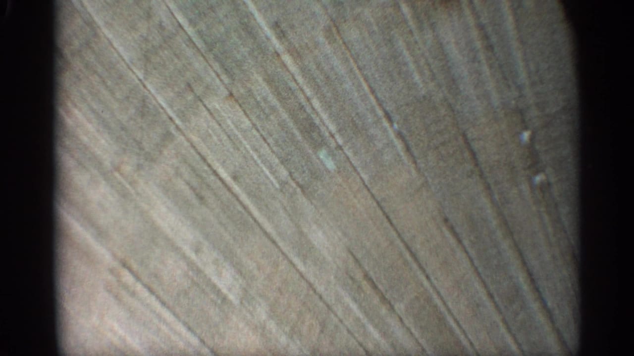 Close 8mm view of a weathered wall surface in the Arizona 1959 clip, with diagonal marks and muted natural light.