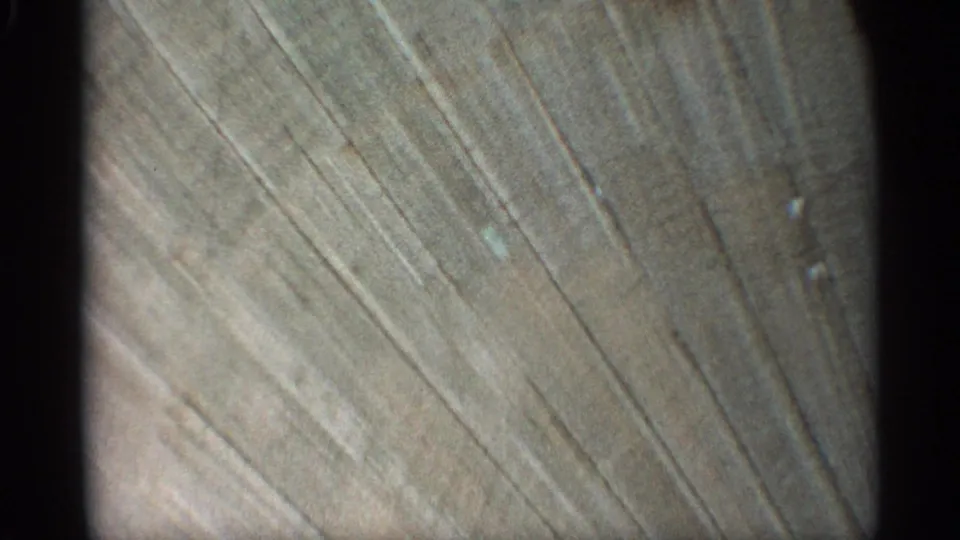 Close 8mm view of a weathered wall surface in the Arizona 1959 clip, with diagonal marks and muted natural light.