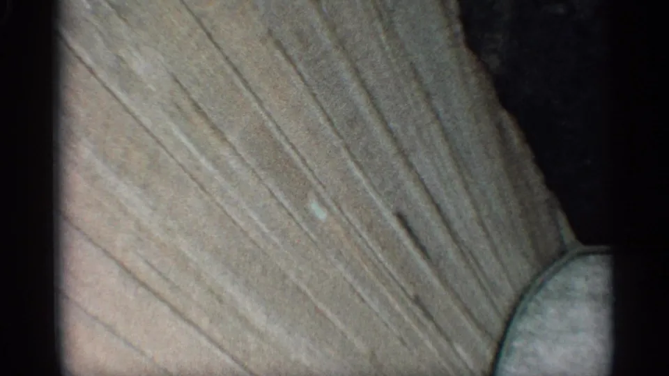 Handheld 8mm frame showing the textured wall at an angle, with a shadowed area and rounded structural edge entering the lower right.