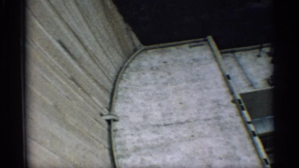 Final 8mm frame from the Arizona clip, showing a textured wall next to a pale rounded architectural form and shadowed space.