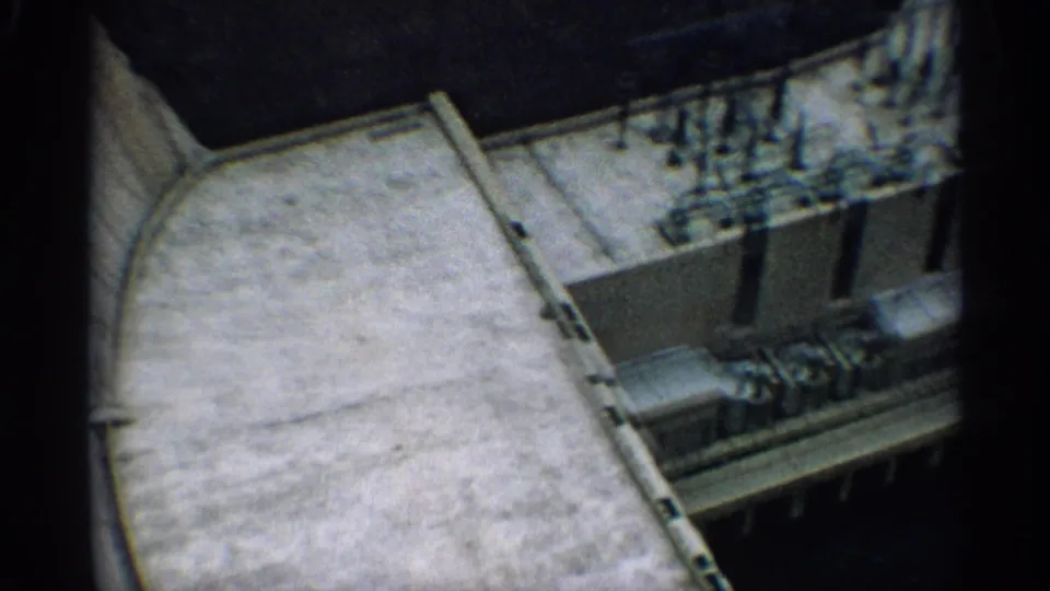 1959 Arizona 8mm frame showing an overhead view of concrete dam construction with equipment lined along a service deck.