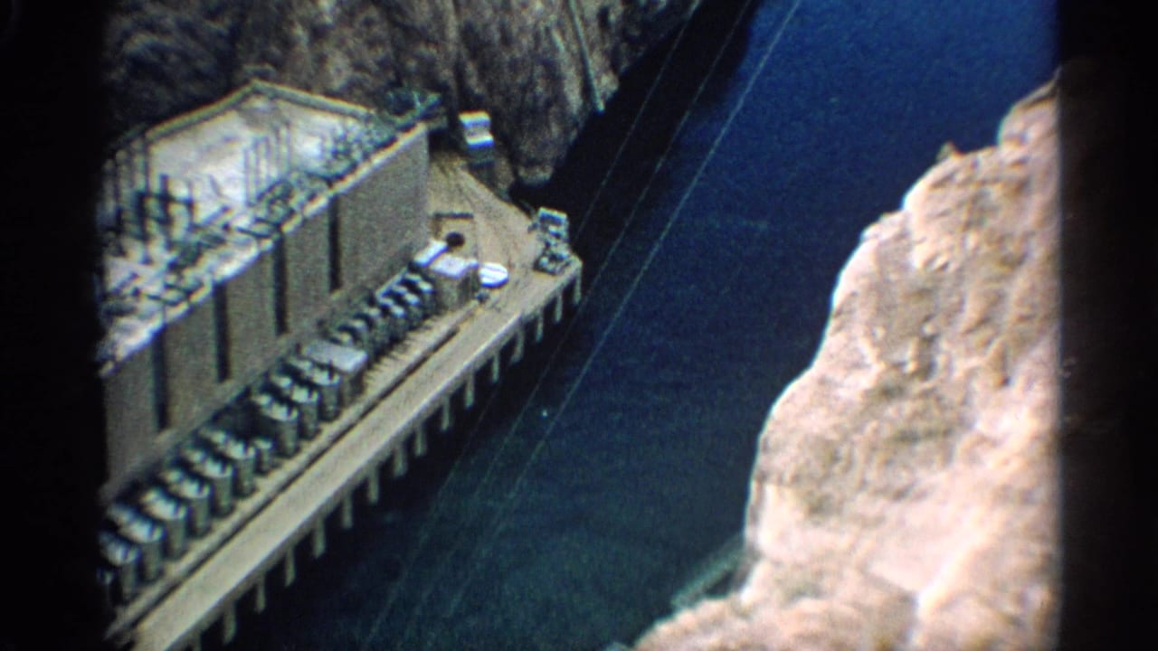 Aerial view of a concrete dam structure beside deep blue canyon water.