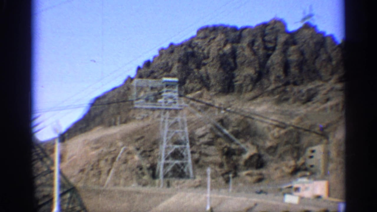 Metal transmission tower and power lines on rocky desert terrain.