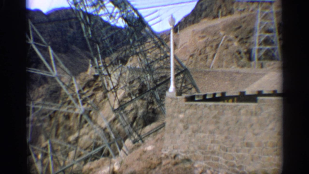 Transmission structures and power lines beside a stone wall in desert hills.