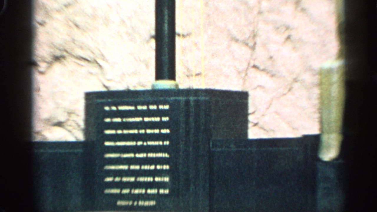 Close view of a dark engraved plaque beside vertical monument elements and a textured wall.