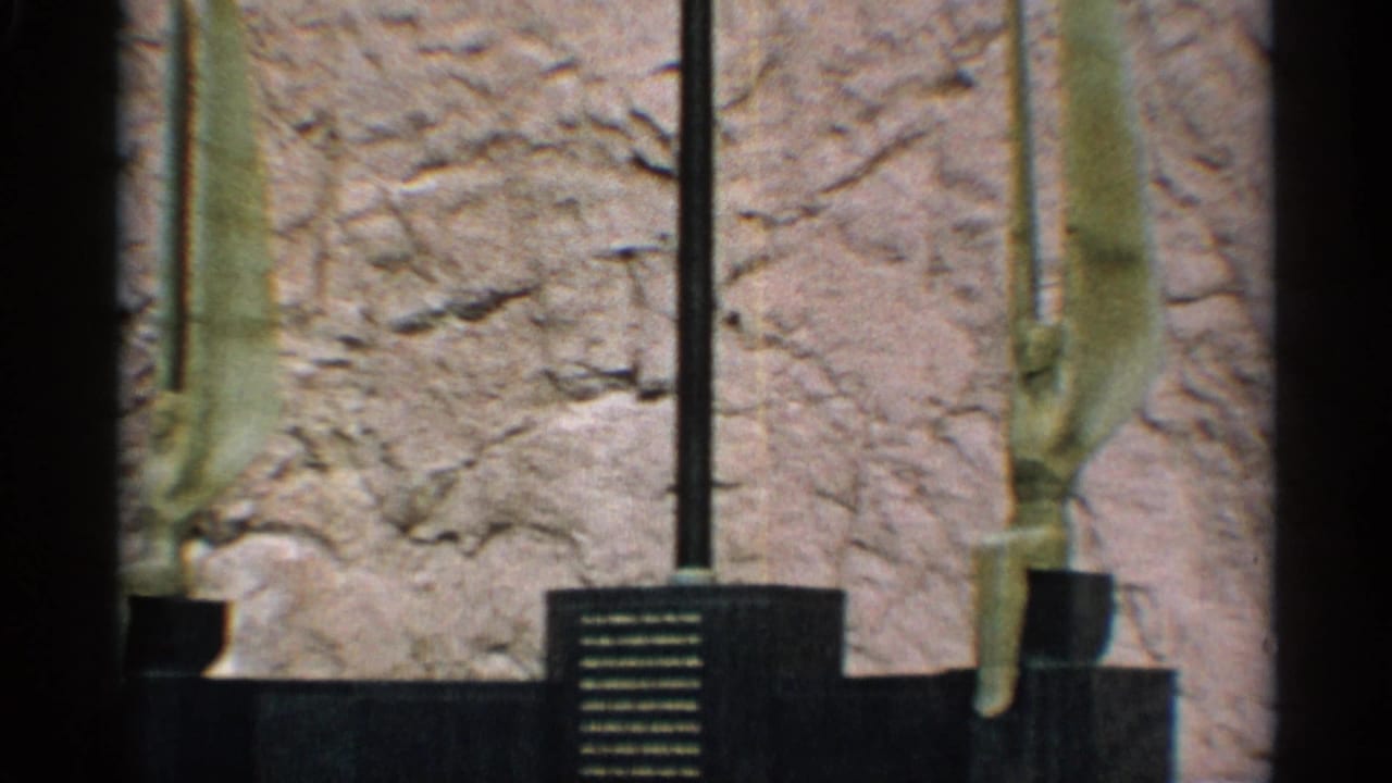 Weathered statue legs and pedestal near a dark plaque against a rough wall.