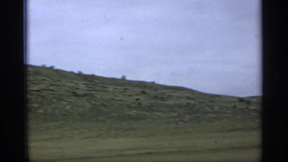 1959 Arizona home-movie frame of a dry hillside seen from a moving vehicle, bordered by dark 8mm frame edges.