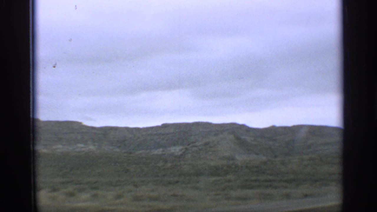 Cloudy sky over green hills seen through dark 8mm frame edges.