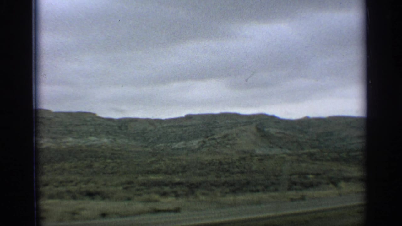 Green hillside landscape beneath a gray sky, framed by dark film edges.