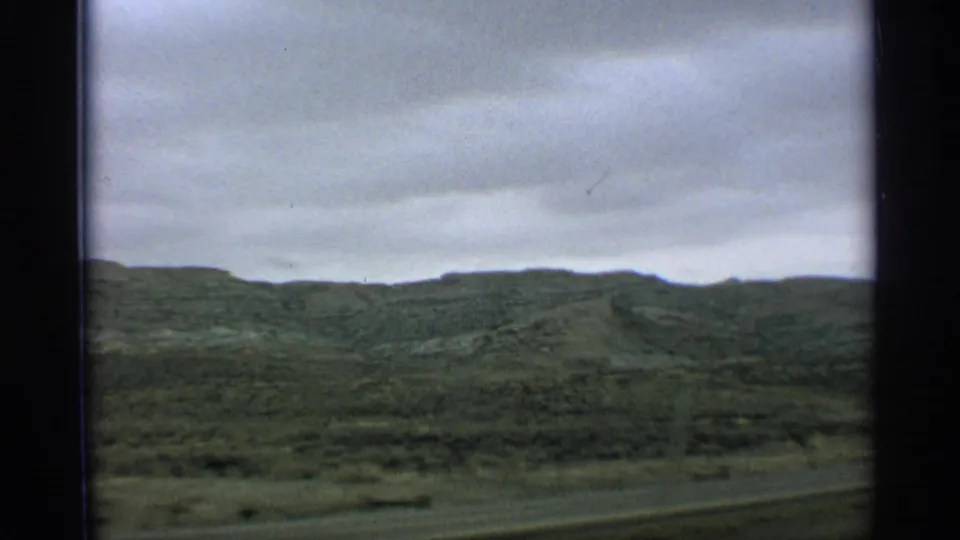Arizona road-trip footage from 1959 shows a broad green hillside and overcast sky with subtle motion blur.