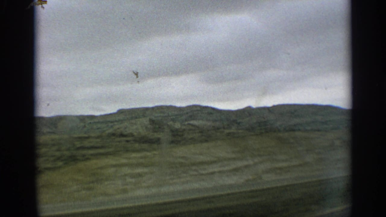 Cloudy sky over rolling green hills seen through a moving vehicle window.