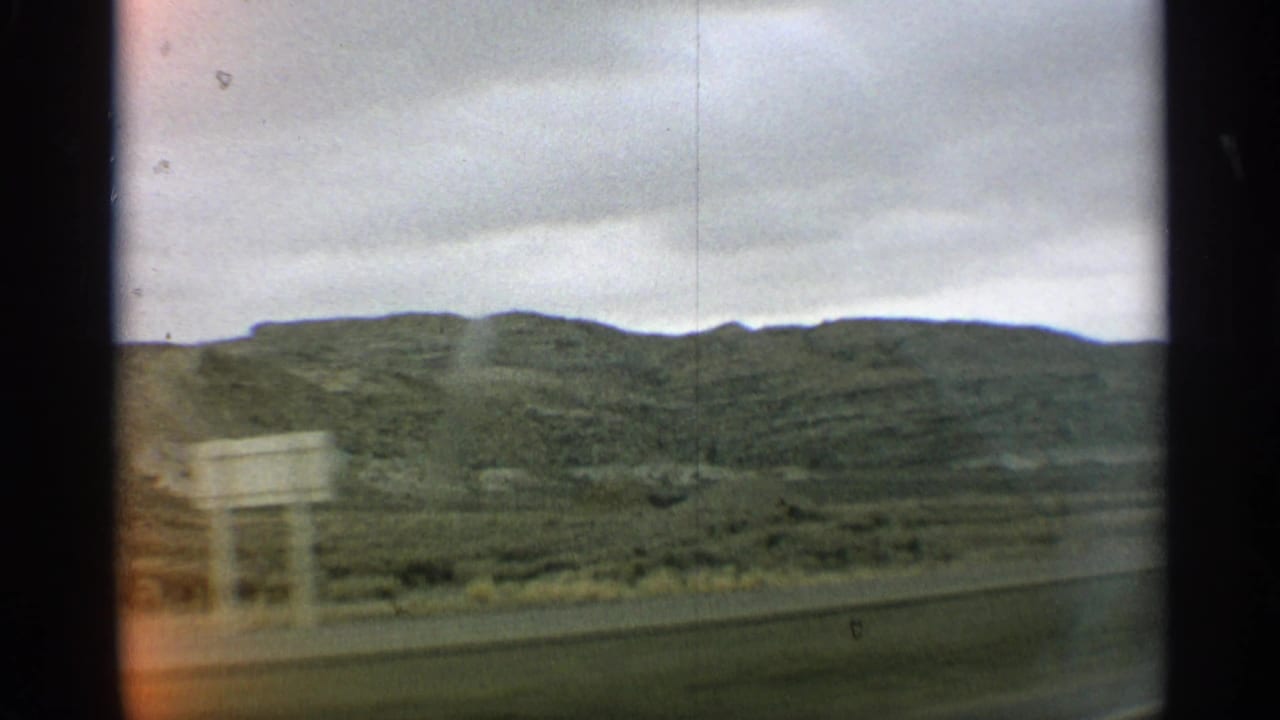 Roadside hills and cloudy sky with a brief pale sign or structure near the road.
