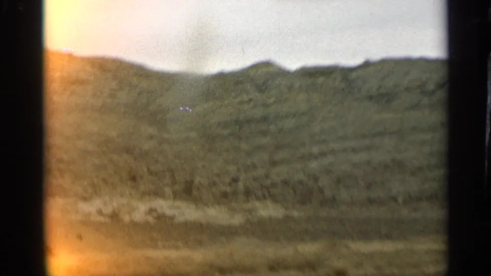 1959 Arizona 8mm frame showing open hills and roadside terrain, with a golden light leak along the edge of the film.
